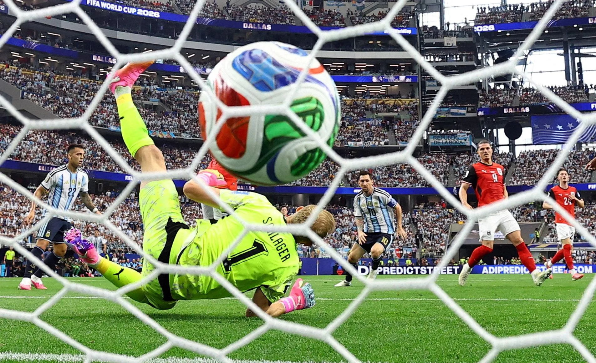 A shot from behind goal showing the ball about to hit the back of the net behind Austria’s goalkeeper Alexander Schlager with Lionel Messi in the backdrop